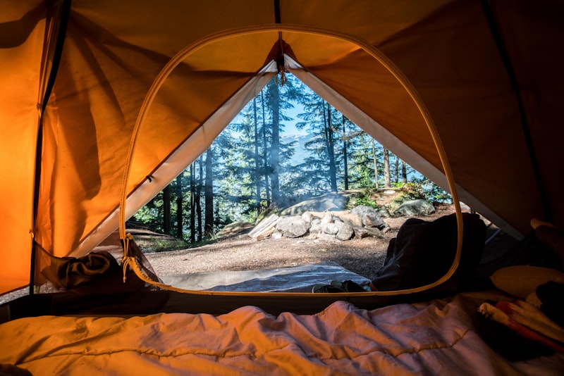 Camping tents pitched near a calm lake with hills in the background at dusk.