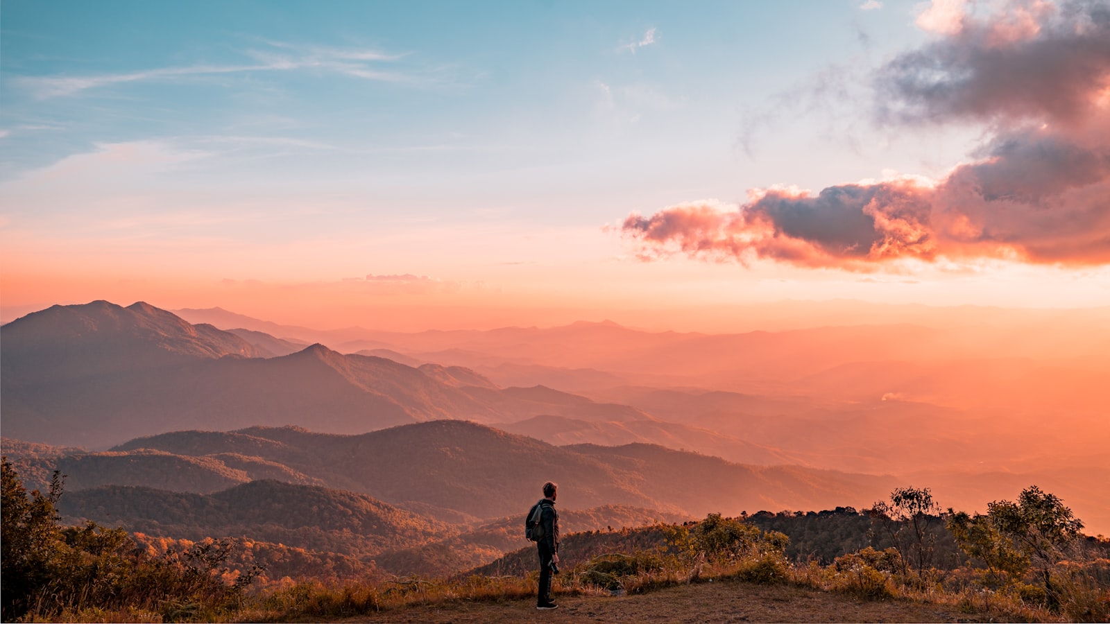 A hiker walking steadily along a mountain trail with valleys behind.