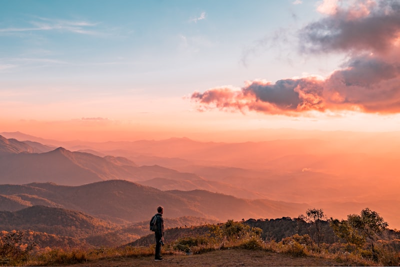 A hiker walking steadily along a mountain trail with valleys behind.