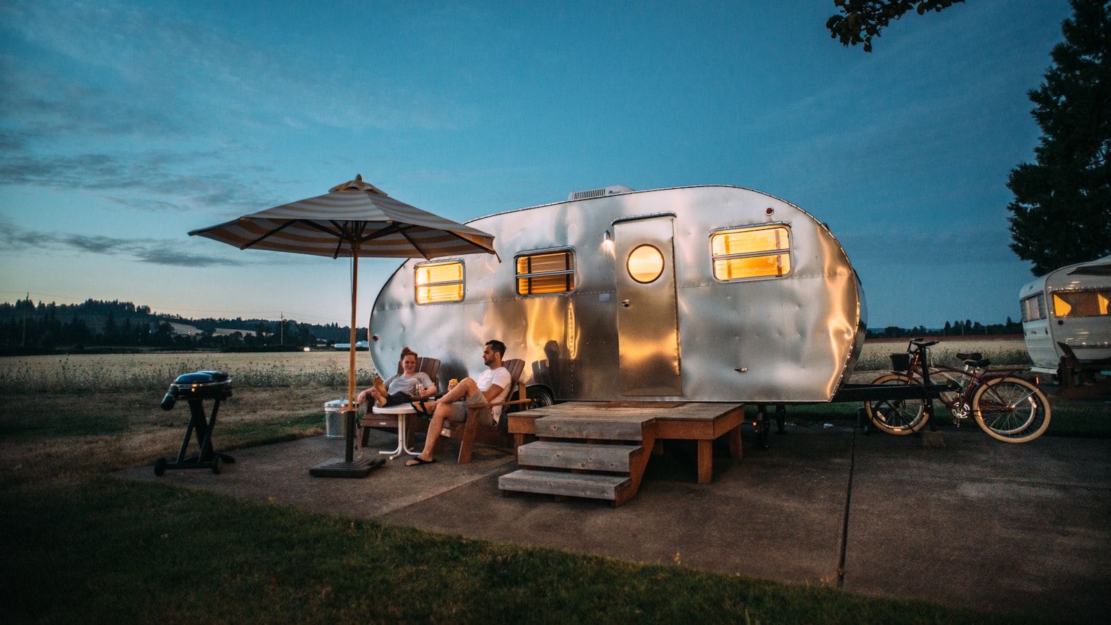 An orange dome tent pitched and staked out on grass at a wooded campsite.