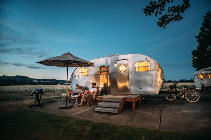 An orange dome tent pitched and staked out on grass at a wooded campsite.