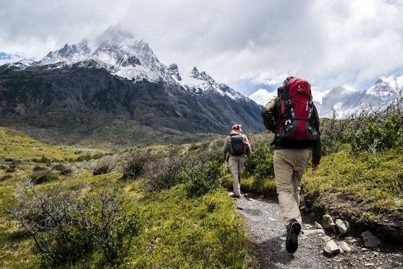 A hiker in layered outdoor clothing standing on a trail with hills behind them.